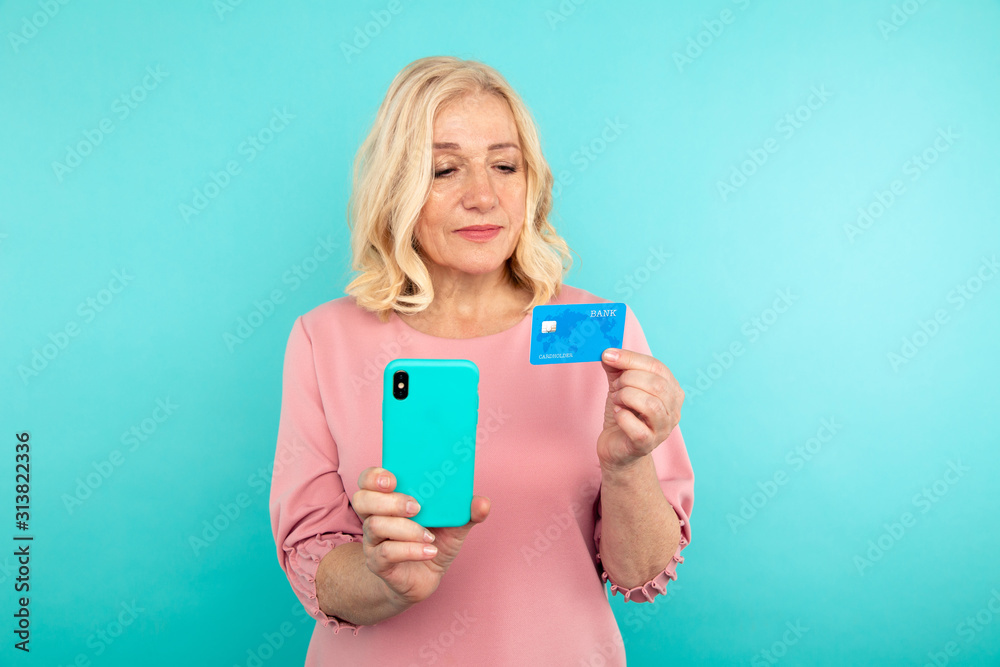 Happy adult female person holding credit card and phone in the blue background Happy adult female person holding credit card and phone in the blue background