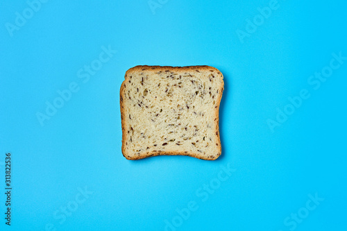 Single square piece of bread with seeds for toast lies on blue table on kitchen. Top view. Close-up