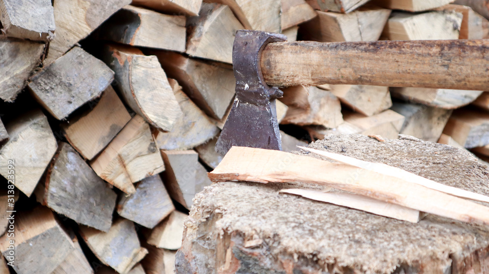 Chipped firewood for the winter for heating. The ax is stabbed with a blade into the stump. Cleaver with a wooden handle. Harvesting on the farm. Dry firewood stacked in piles for heating a house Chipped firewood for the winter for heating. The ax is stabbed with a blade into the stump. Cleaver with a wooden handle. Harvesting on the farm. Dry firewood stacked in piles for heating a house