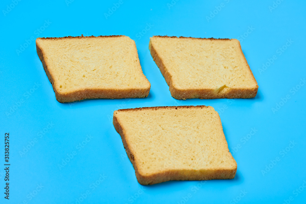 Fototapeta premium Three square pieces of yellow vanilla bread for toast lies on blue table on kitchen. Close-up