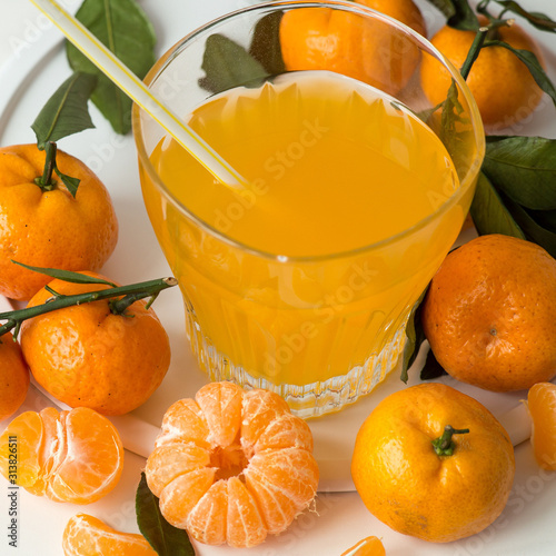 A glass with freshly made juice and juicy ripe tangerines on a light background. Source of natural vitamins. Selective focus.