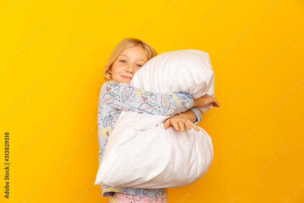 Adorable little girl looking at the camera and hugging a pillow background of a yellow wall. Adorable little girl looking at the camera and hugging a pillow background of a yellow wall.
