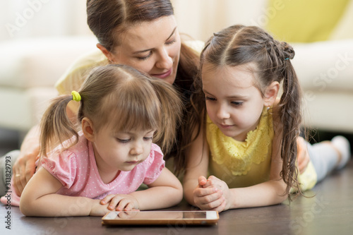 Preschool children and their mom lying on floor in living room with tablet pc