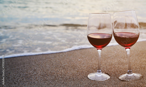 Wine glasses with red wine on sand on the beach. Valentine's Day concept.