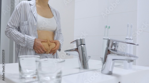 Woman With Postpartum Belly Looking At The Mirror In Bathroom.