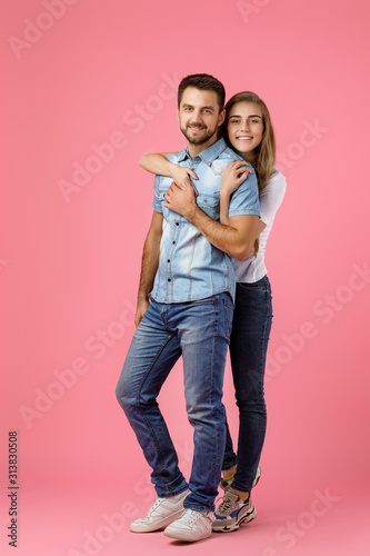beautiful happy couple in love in denim wear are hugging and looking at camera on pink background. st valentines day