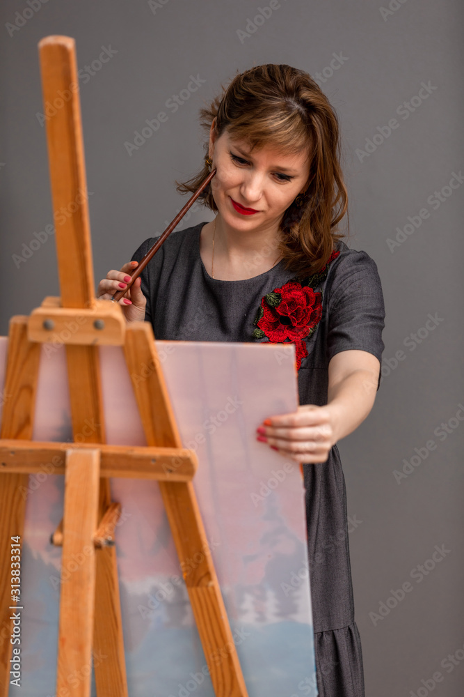 Portrait of a young artist girl who draws picture behind an easel. The concept of hobby, creative rest. Portrait of a young artist girl who draws picture behind an easel. The concept of hobby, creative rest.