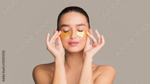 Foto Young woman applying golden collagen patches under eyes