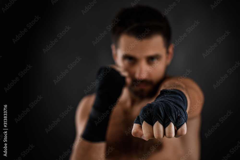 boxer man with bandage on hands training before fight and showing the different movements on black background. focus on hand