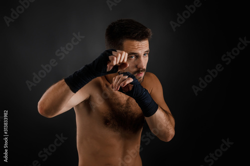 boxer man with bandage on hands was hit and he defends himself on black background