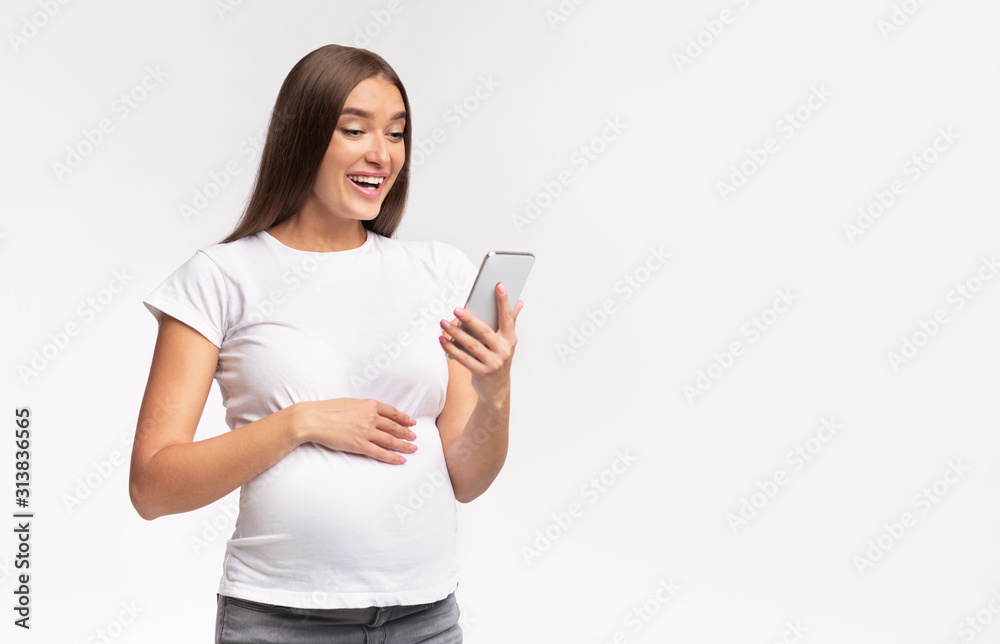 Happy pregnant woman using smartphone standing over white studio background Happy pregnant woman using smartphone standing over white studio background