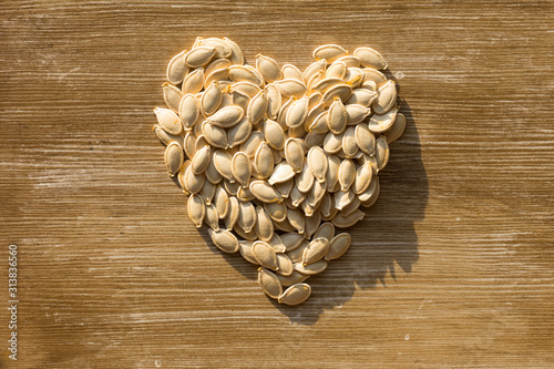 Top view of raw seeds pumpkin in shape of heart on the wooden background. Concept healthy for heart.