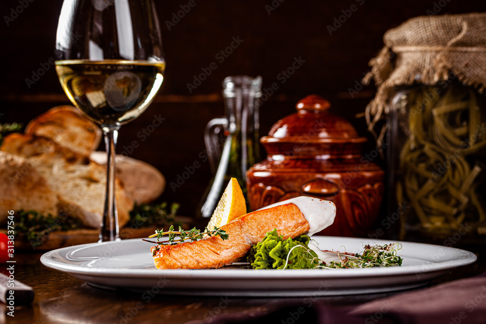 Italian Cuisine. Red fish steak, salmon with lemon, a side dish of spinach. Beautiful restaurant serving in a white plate with a glass of white wine. background image, copy space