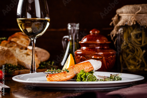 Italian Cuisine. Red fish steak, salmon with lemon, a side dish of spinach. Beautiful restaurant serving in a white plate with a glass of white wine. background image, copy space
