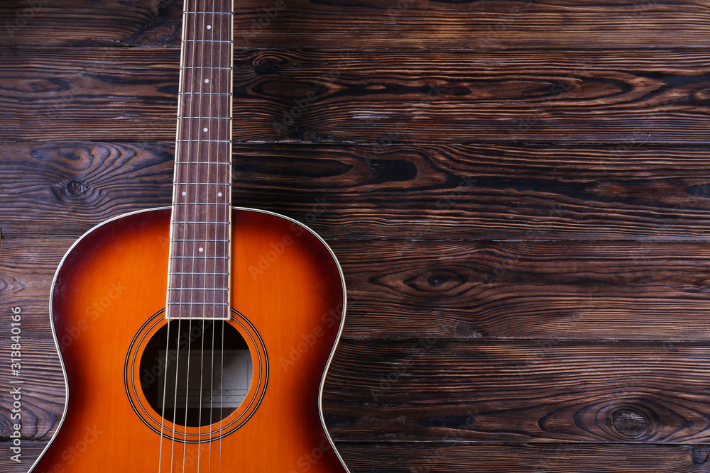 Obraz premium Cropped image of vintage style travel size acoustic guitar with rosewood neck and no pickguard on grunged dark wood textured background. Close up, copy space for text, top view.