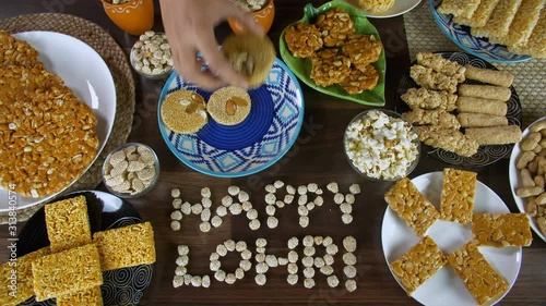 Woman hands serving til patti in a blue ceramic plate for the Lohri festival in India. Top view shot of 'Happy Lohri' text written with rewri and surrounded by Lohri items like gajak  peanuts chikk... photo