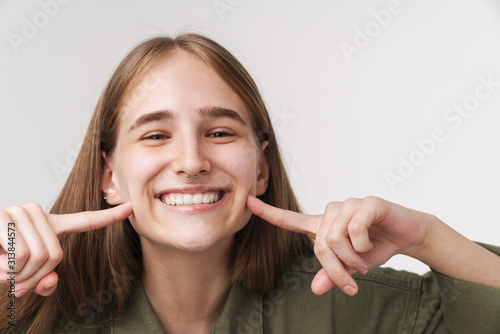 Fototapeta Naklejka Na Ścianę i Meble -  Photo of funny caucasian woman pointing fingers at cheeks and smiling