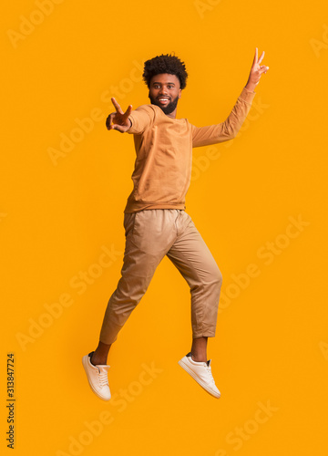 Active black man gesturing peace while jumping in the air