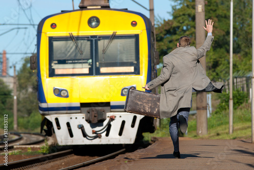 A man is trying to catch a train. Man is late for train. Man is running behind a train and waving his hand. 