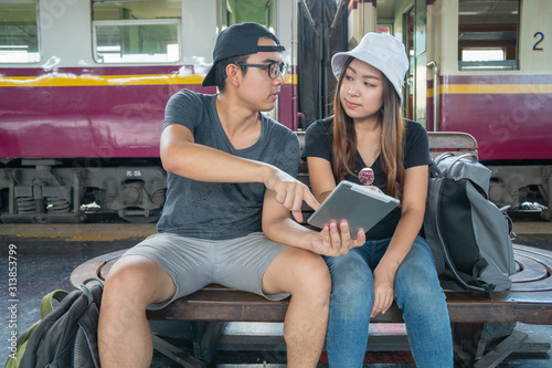 Young asian couple backpacker using tablet for find destination trip at railway station