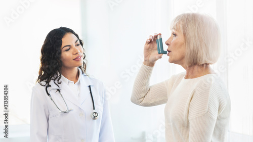 Physician examining mature woman using blue asthma inhaler photo