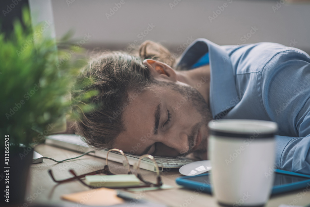 Obraz premium Young bearded man in blue shirt having a nap at work