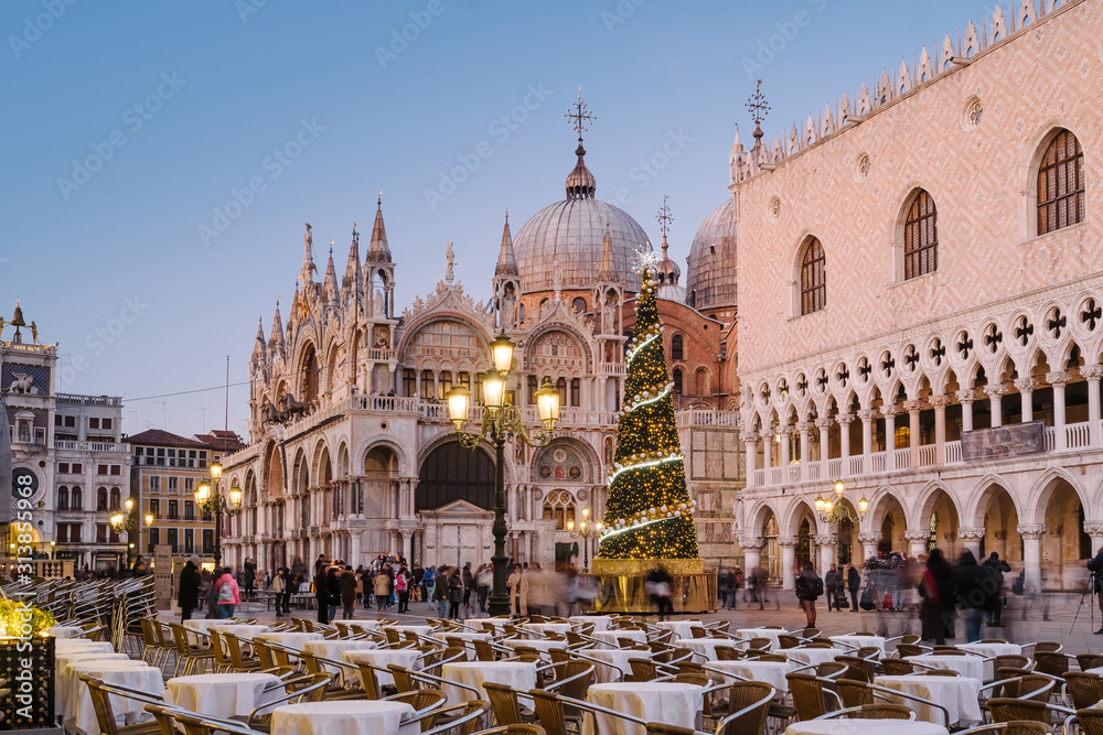 Venice, Italy, 23 December 2019 - People walking in San Marco square in the evening. On the square the Christmas tree with lights and decorations in front of the Doge's Palace