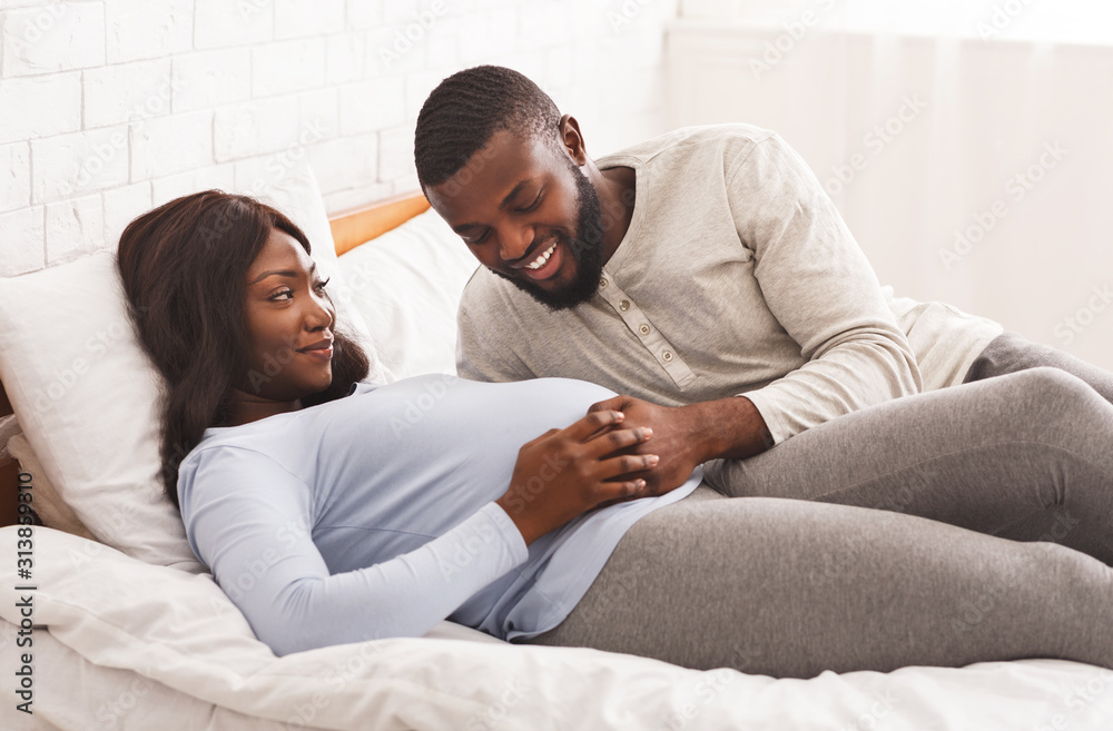 Happy young pregnant couple cuddling in bed at home
