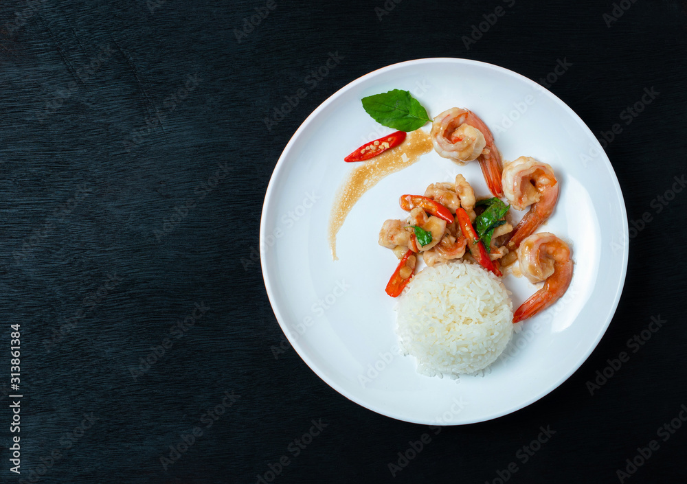 Stir fried shrimp with basil and rice on a white plate, on a black wooden floor Stir fried shrimp with basil and rice on a white plate, on a black wooden floor