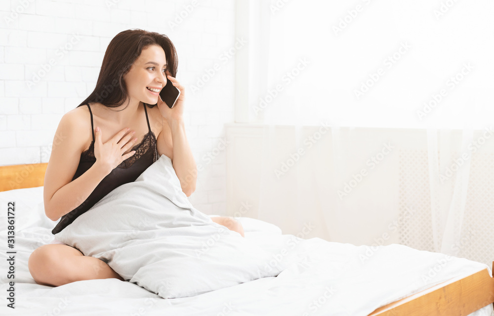 Happy girl in pajamas talking on mobile phone in bed Happy girl in pajamas talking on mobile phone in bed