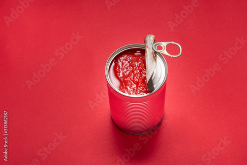 Opened tin can with canned tomatoes, on red background © mdbildes