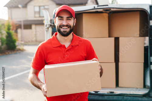 Image of smiling young delivery man standing with parcel box photo