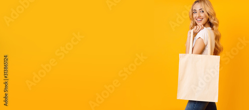 Beautiful blonde girl with tote bag over yellow background, long banner