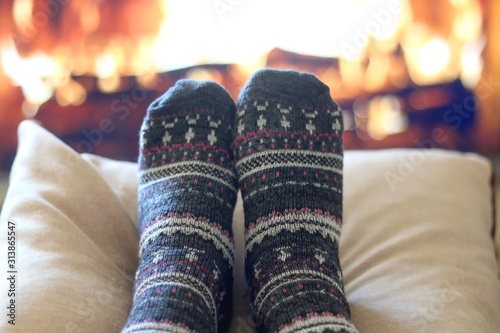 Feet in woolen patterned socks resting by the fireplace. Selective focus.