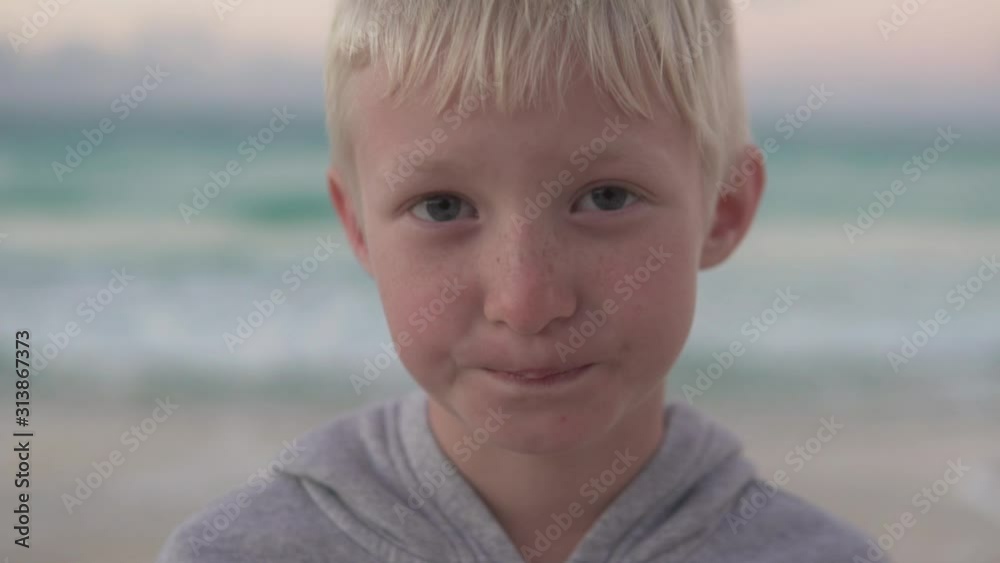 Close-up of a beautiful blond boy against the backdrop of a washed-out sea. Boy albino smiles cutely Close-up of a beautiful blond boy against the backdrop of a washed-out sea. Boy albino smiles cutely