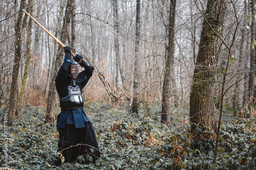 Man practicing kendo with shinai bamboo sword on forest background. Place for text or advertising © Andriy