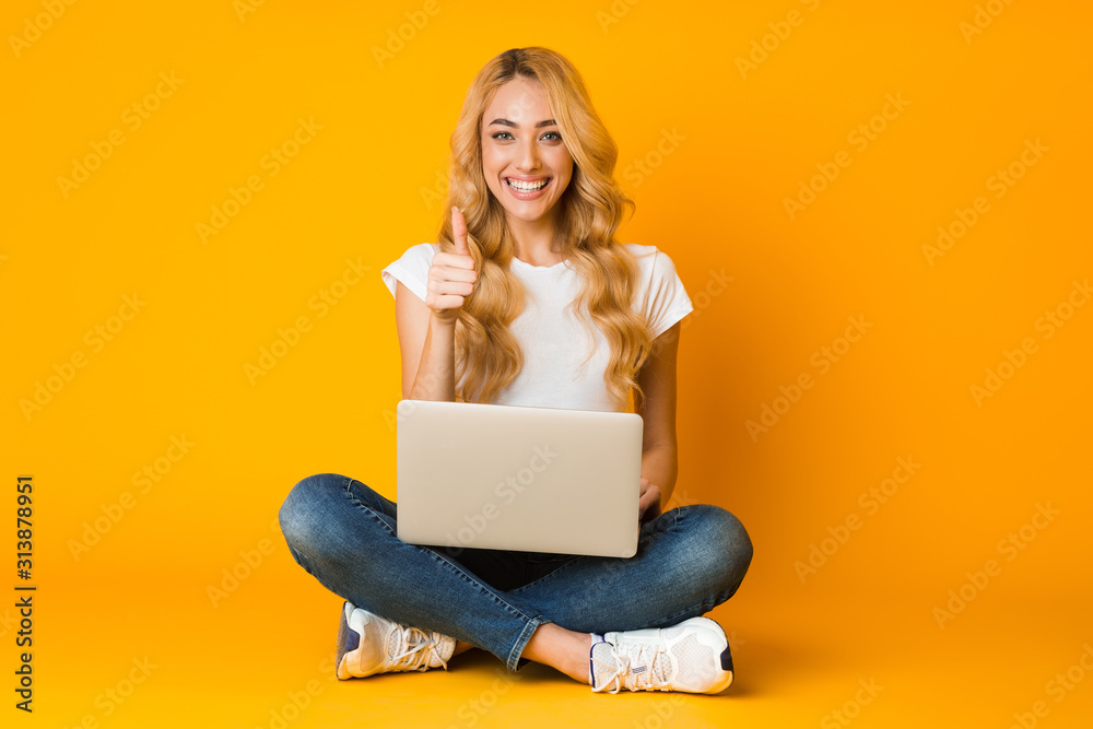 Naklejka premium Cheerful woman using laptop and showing thumb up