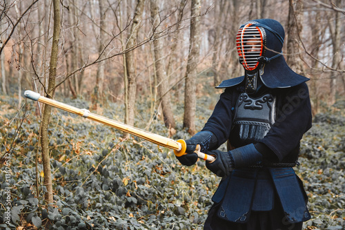 Man practicing kendo with shinai bamboo sword on forest background. Place for text or advertising