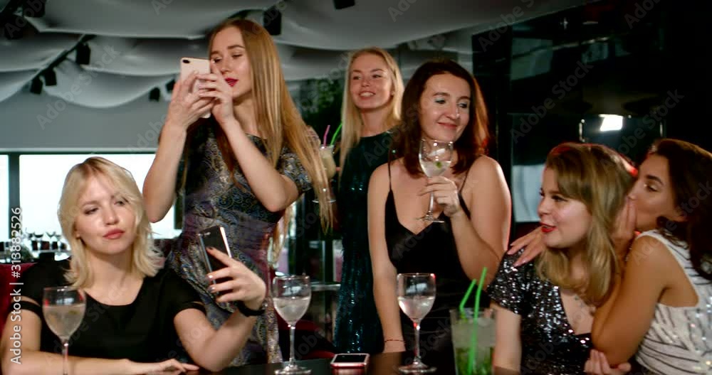 a group of girls in shiny dresses near the cocktail table. they sit, stand, dance, hug, laugh, take selfies a group of girls in shiny dresses near the cocktail table. they sit, stand, dance, hug, laugh, take selfies