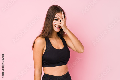 Young caucasian fitness woman doing sport isolated blink at the camera through fingers, embarrassed covering face. © Asier