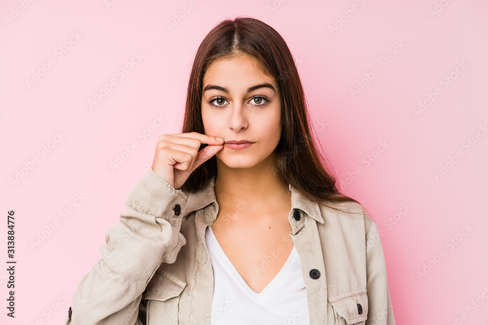 Young caucasian woman posing in a pink background with fingers on lips keeping a secret. Young caucasian woman posing in a pink background with fingers on lips keeping a secret.