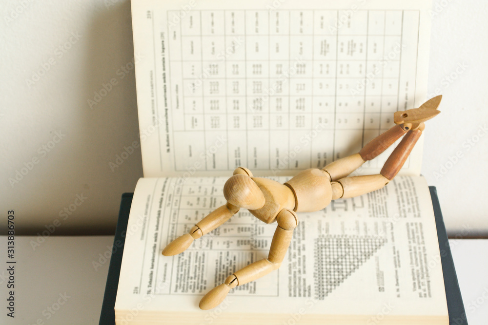 Obraz premium Wooden mannequin manikin lie down on open book and learning with pleasure. He is thinking of mastering the material. A metaphor for studying. Good student. Interest in learning. Education. PhD studies
