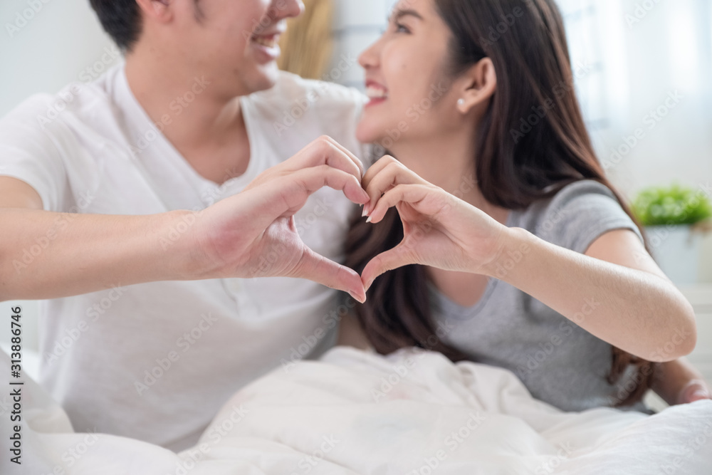 Close up couple hand doing heart gesture together by hands and smiling on white bed in bed room