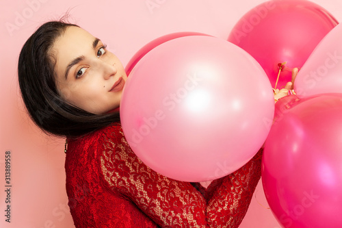 Young pretty woman in red evening dress holding festive air balloons. Portrait of happy 20s middle-eastern female celebrating valentines day, birthday, party