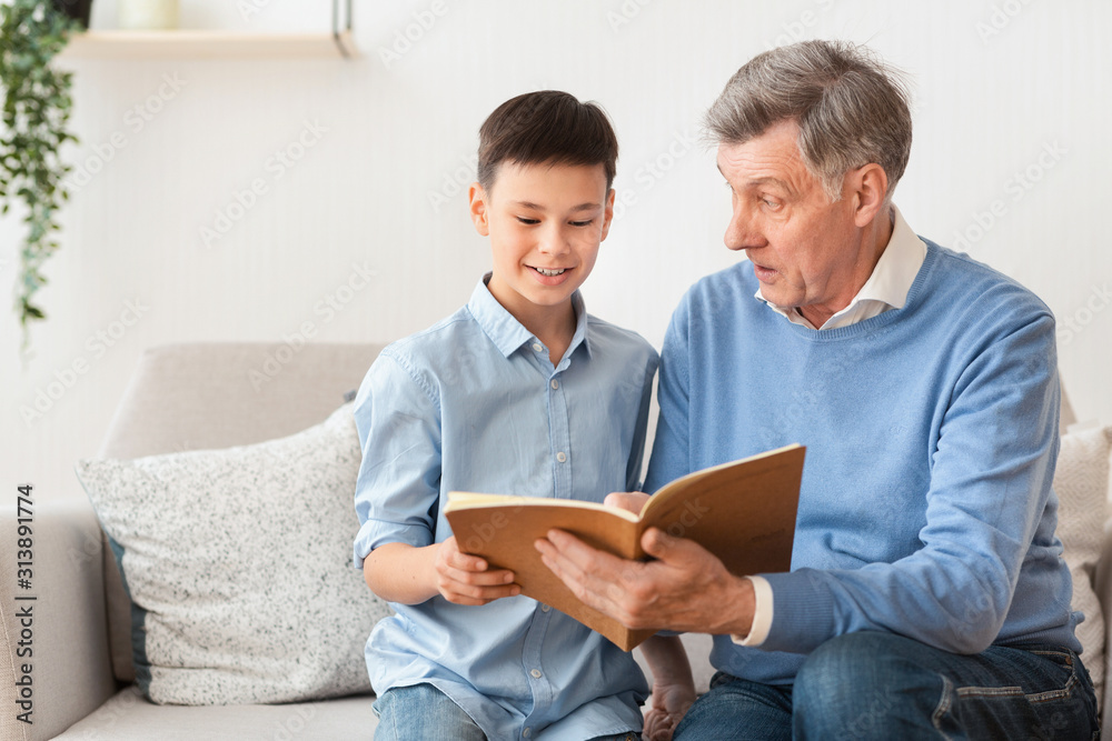 Grandfather And Grandson Reading Book Sitting On Sofa At Home Grandfather And Grandson Reading Book Sitting On Sofa At Home