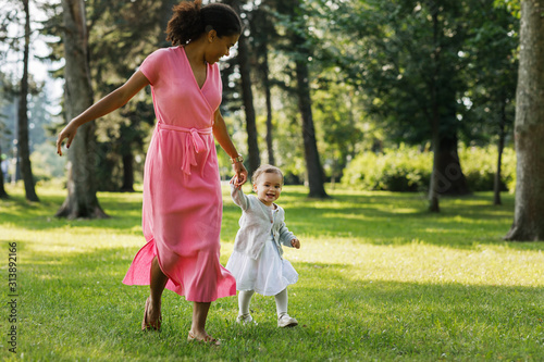 Young woman running with little girl in the park. Mother and daughter holding hands while walking outdoors.