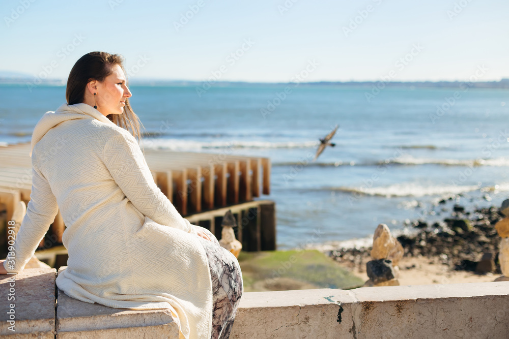 The girl sits on a stone fence. she admires the river view