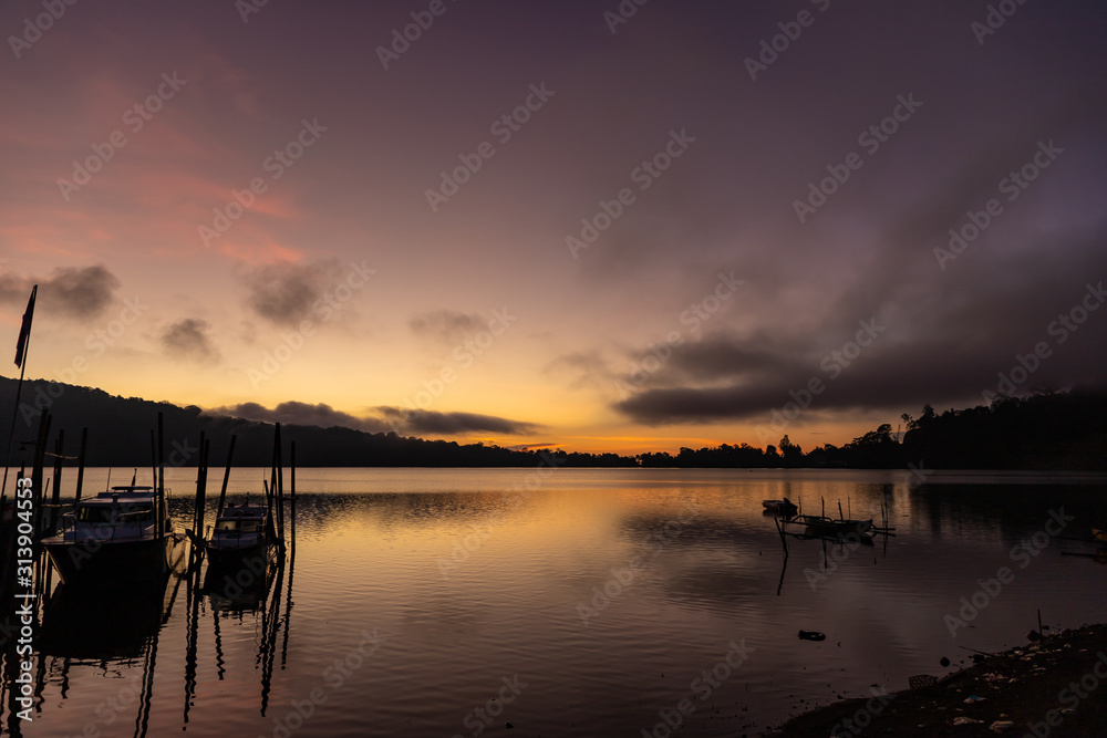 A beautiful sunrise at a Lake Bratan with traditional fishing boats in foreground. Bali island, Indonesia.