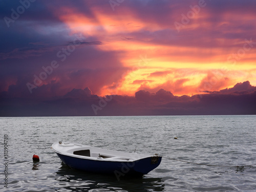 Lonely white and blue sea motor boat and red buoy on water surface side view on sunset