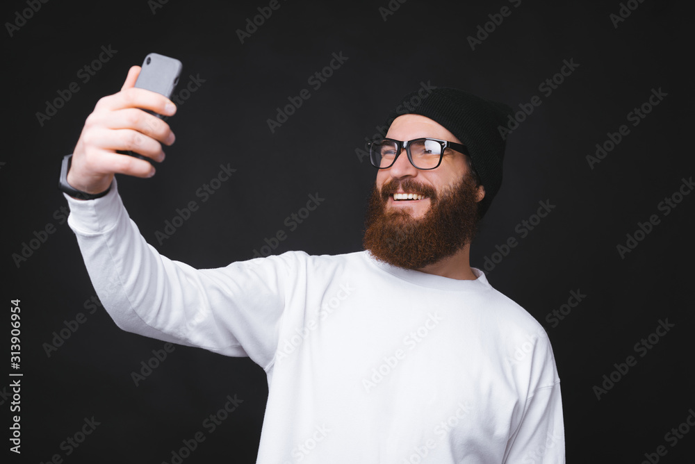 Happy bearded hipster man taking selfie over dark background Happy bearded hipster man taking selfie over dark background